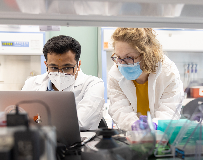 A man and a woman in lab coats working at a computer.
